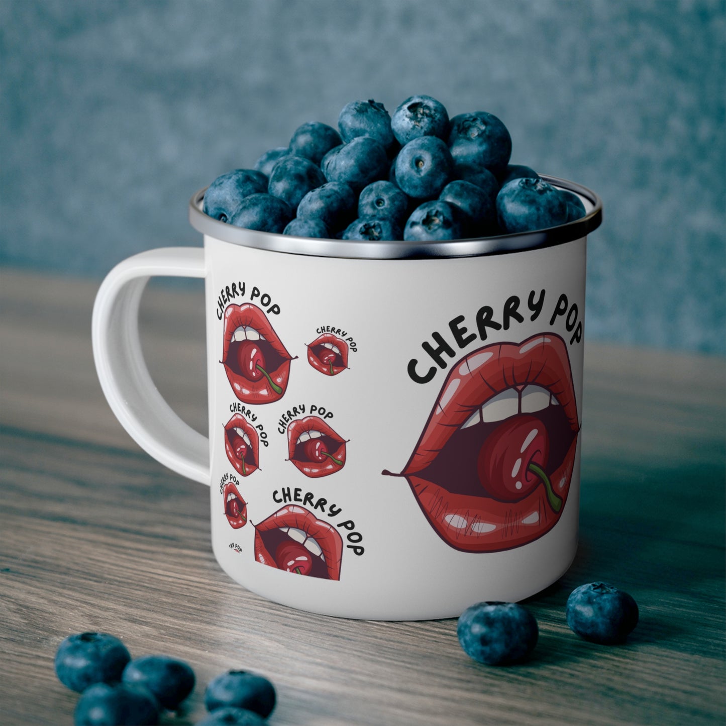cherry pop lips on a white enamel mug filled with blue berries standing on top of a wooden table