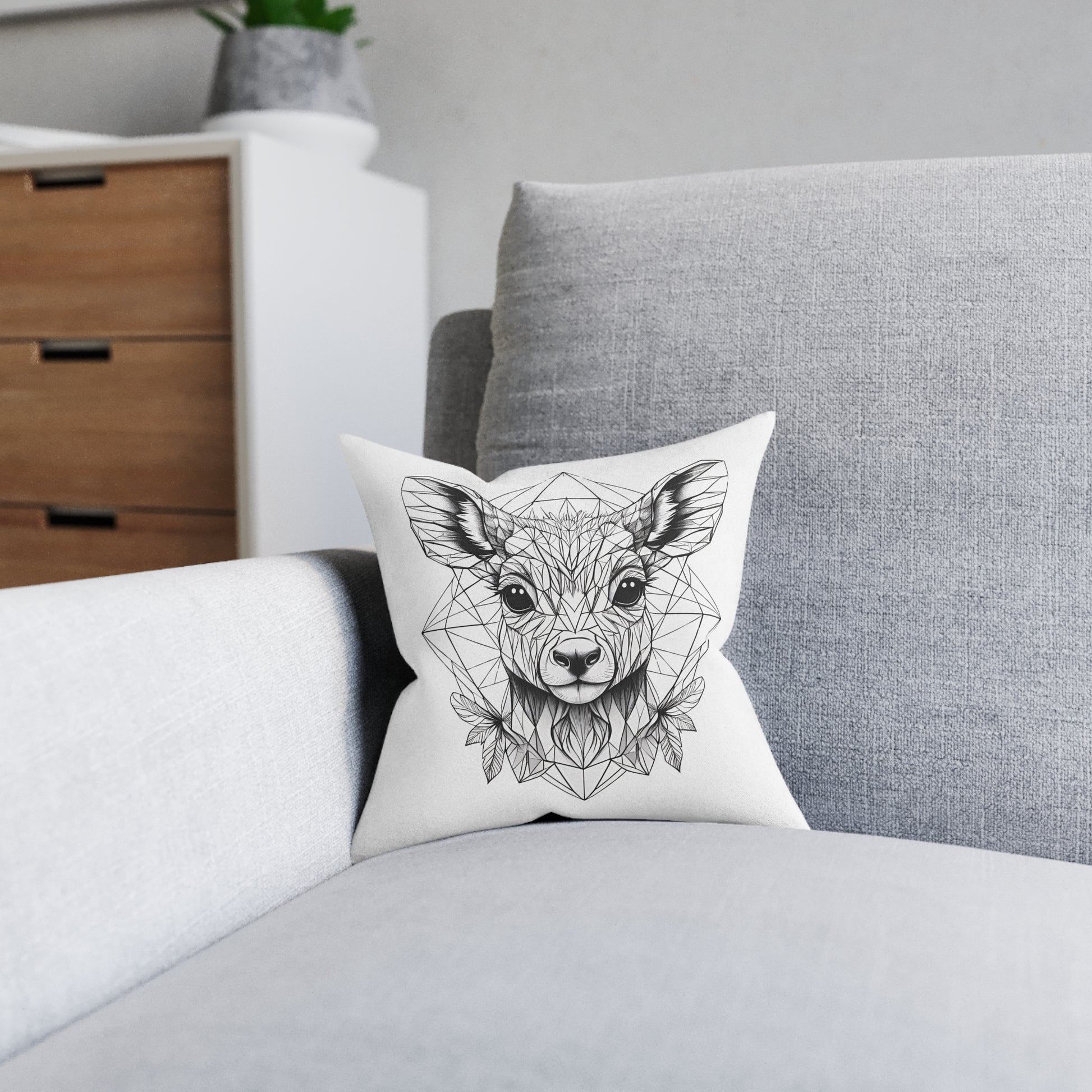 Decorative_white_pillow_with pink backing Polypropylene (faux suede) cover and polyester filling with_a_geometric_deer_design_on_a_gray_sofa