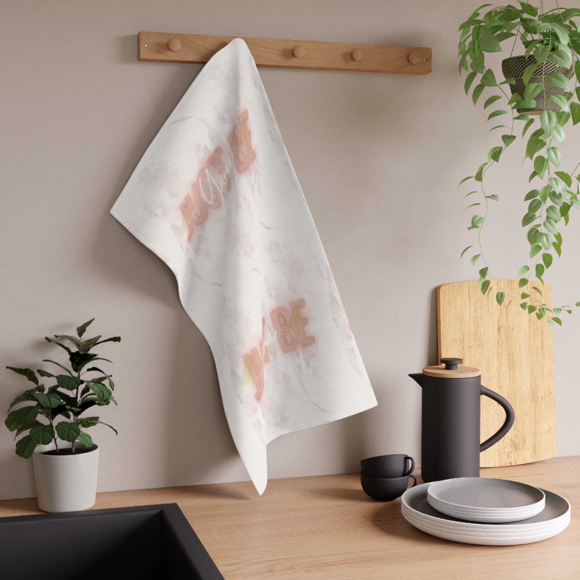 White tea towel with floral pattern  'Just Be You" design hanging on a wooden rack in a kitchen setting.